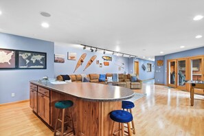Een ruime woonkamer met een centraal eiland, houten barkrukken, een bank en een eettafel.