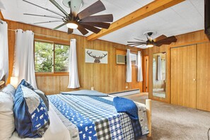 Een slaapkamer met een bed, houten wanden, een plafondventilator, een raam en een deur.