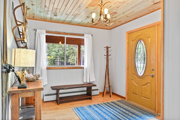 Een kamer met een houten bank, een houten deur met een ruit, een houten plafond, en een bank met een lamp en decoratieve objecten.