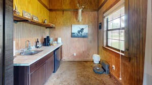 A rustic kitchen with wooden walls, a mounted deer head, a coffee maker, wine glasses, and a window with a view. - VIP Cabin A w/ Lake Views & Private Lake Access with Dock (Ingram)