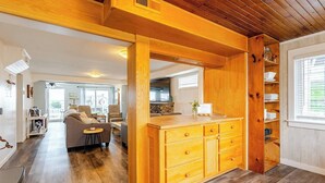 Een ruime keuken met houten kastjes en een centraal eiland, een gezellige zithoek met een bank en een eettafel, en uitzicht op de omgeving door grote ramen.