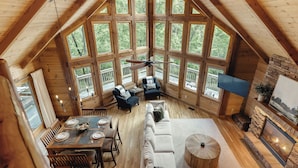 Un amplio loft con techo alto, ventanas grandes, ventilador de techo, chimenea y zona de comedor.