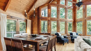 Un interior espacioso de madera con comedor, asientos y ventanas amplias.