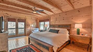 Quarto de cabana de madeira com uma cama, mesa de cabeceira, cadeira, janela e ventilador de teto.