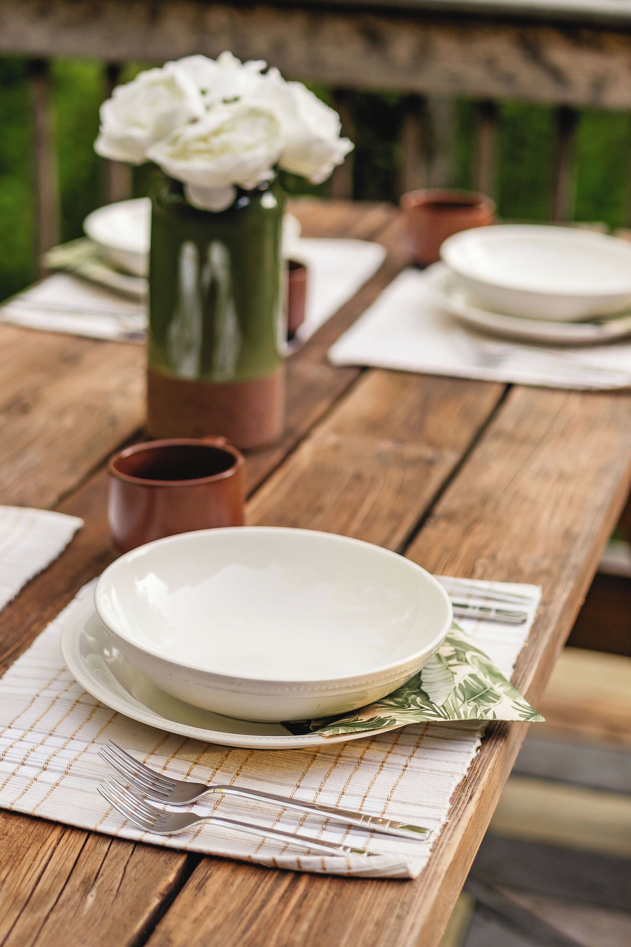 A wooden table set with plates, a cup, and a vase with flowers.