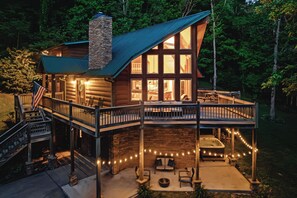 Une cabane en rondins avec un balcon, un jacuzzi et des guirlandes lumineuses.