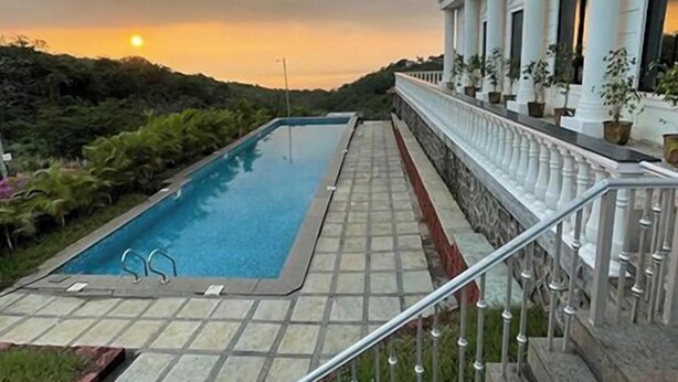 A swimming pool with a stone deck, a staircase leading to a balcony with columns, and a sunset in the background. - BLUE BREEZE (Dapoli)