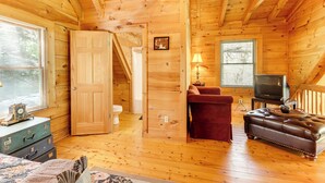 Una cabaña acogedora con paredes y suelos de madera, un televisor, un sillón rojo y un otoman de cuero.