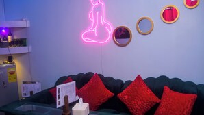A room with a neon sign, a mirror, and red pillows on a green couch.