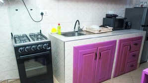 A kitchen with a gas stove, oven, sink, and pink cabinets.