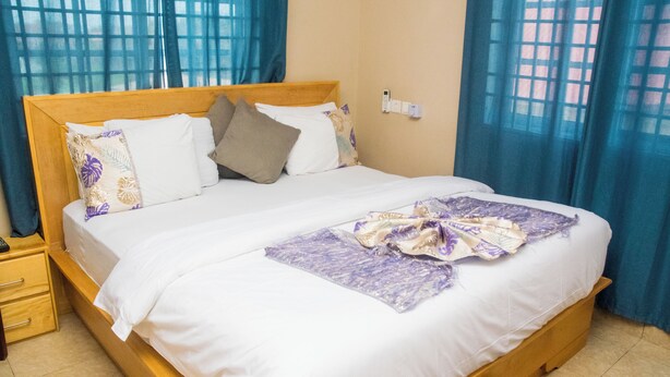 A neatly made bed with white linens and a purple blanket, a wooden headboard, and a nightstand with drawers.