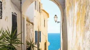 Une ruelle pavée étroite menant à un bâtiment d’où l’on a vue sur la mer.