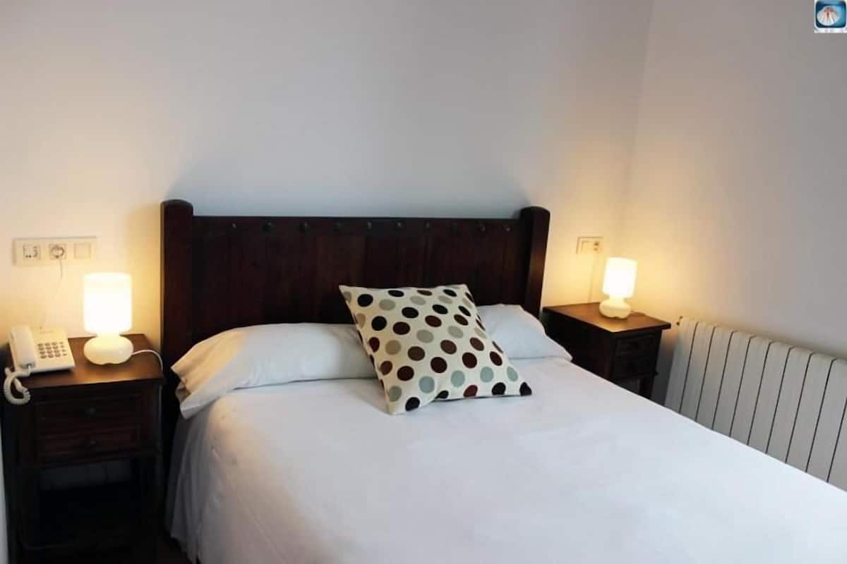 A hotel room with a single bed, a wooden headboard, bedside lamps, a telephone, and a radiator.