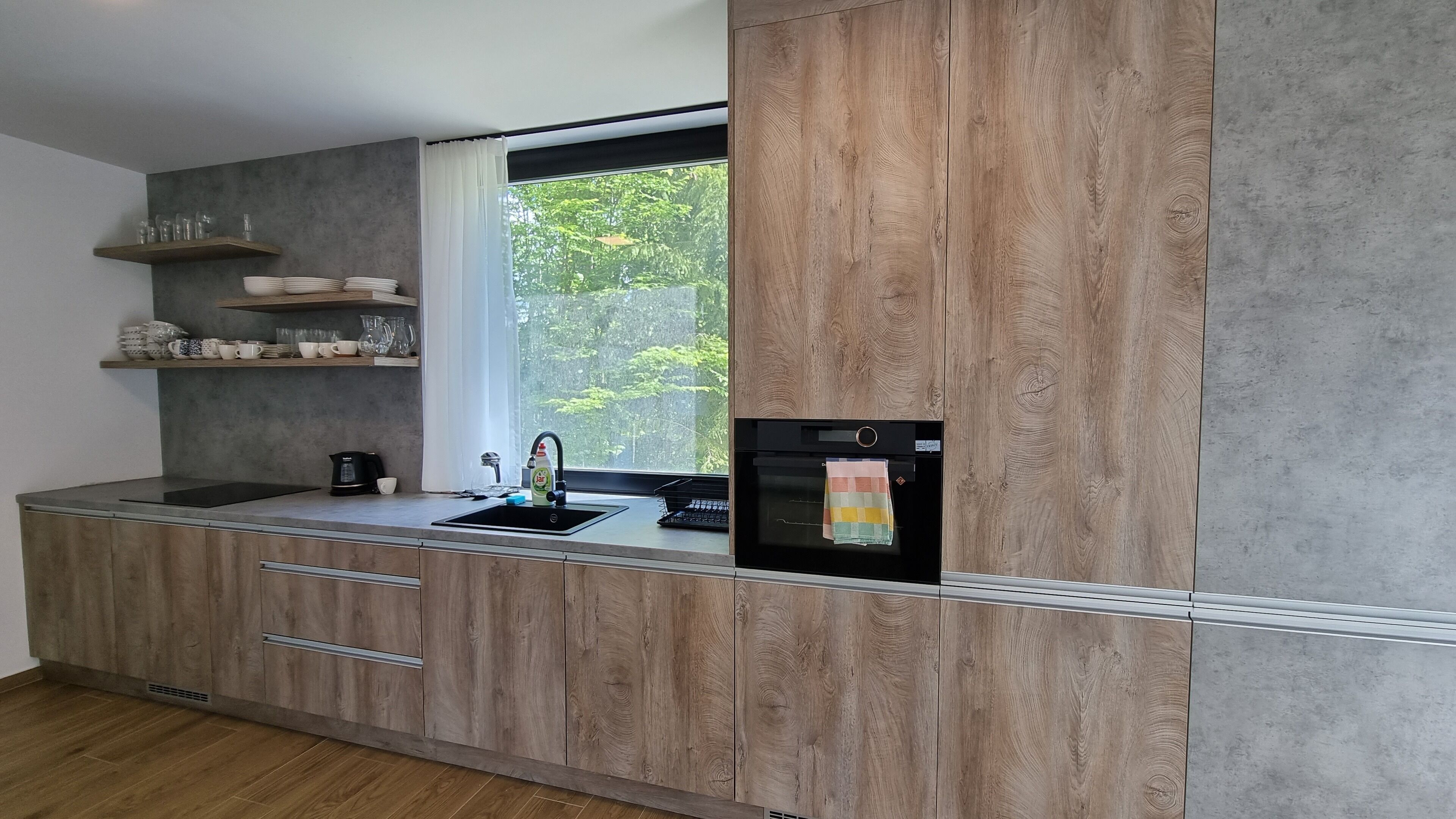 Una cocina moderna con armarios de madera, horno empotrado y ventana con vistas a la vegetación.