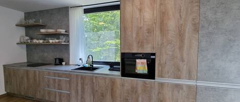 Una cocina moderna con armarios de madera, horno empotrado y ventana con vistas a la vegetación.