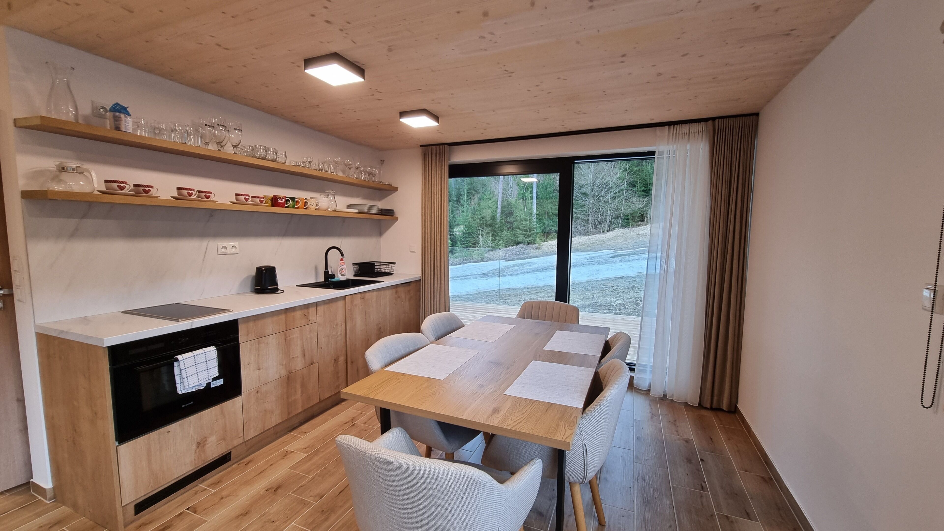 Een moderne keuken met houten kasten, een inbouwoven en een eethoek met een grote tafel en stoelen.