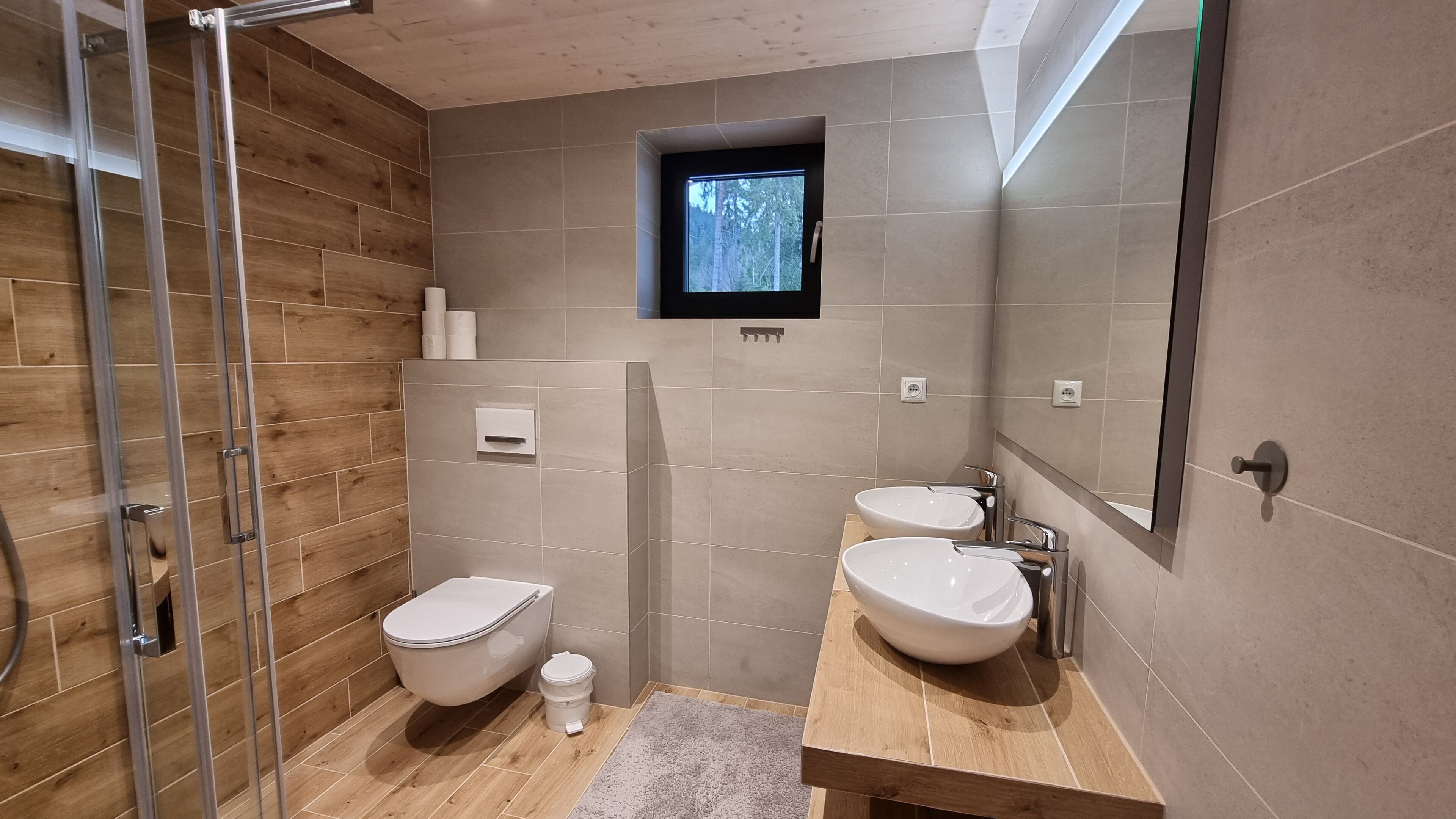 A modern bathroom with a wooden floor, two sinks, a toilet, and a shower.