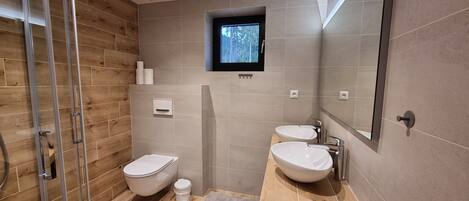 A modern bathroom with a wooden floor, two sinks, a toilet, and a shower.