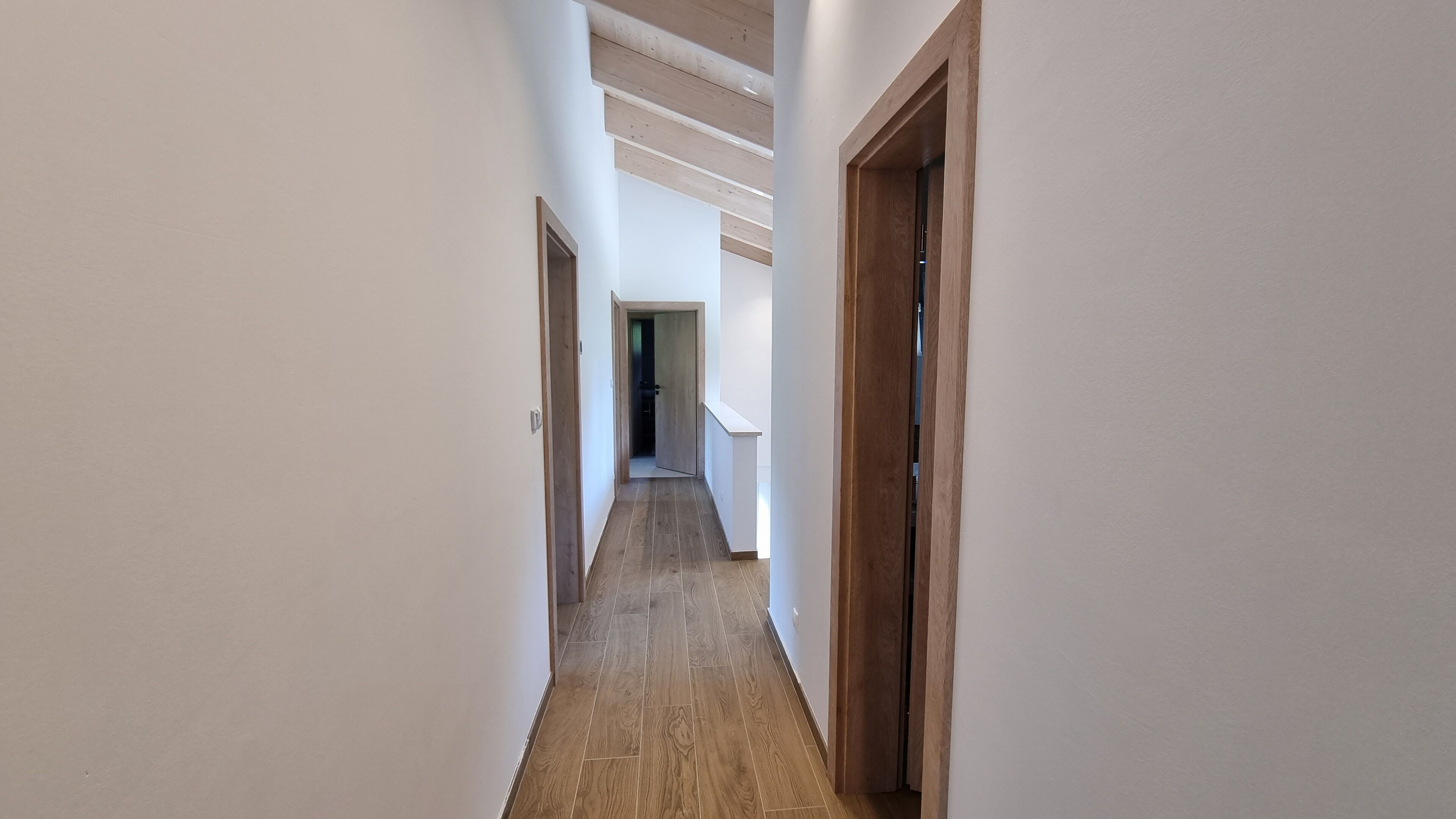 A narrow hallway with wooden flooring and white walls.