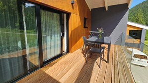 A modern outdoor deck with a wooden floor, a glass table with chairs, and a vase of flowers. - Chalets Hrabovo (Ruzomberok)