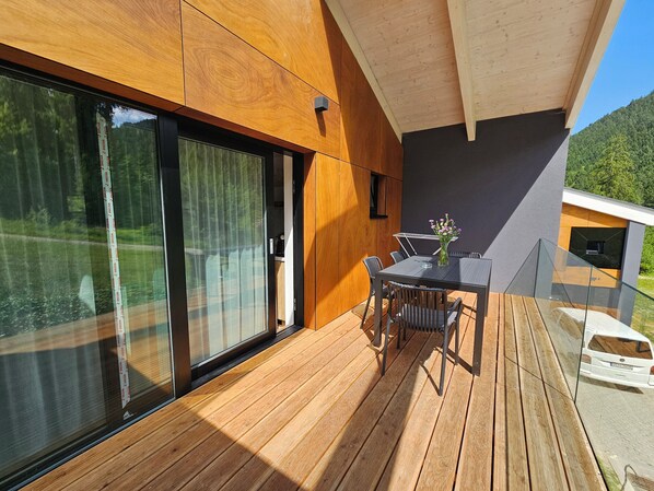 A modern outdoor deck with a wooden floor, a glass table with chairs, and a vase of flowers. - Chalets Hrabovo (Ruzomberok)
