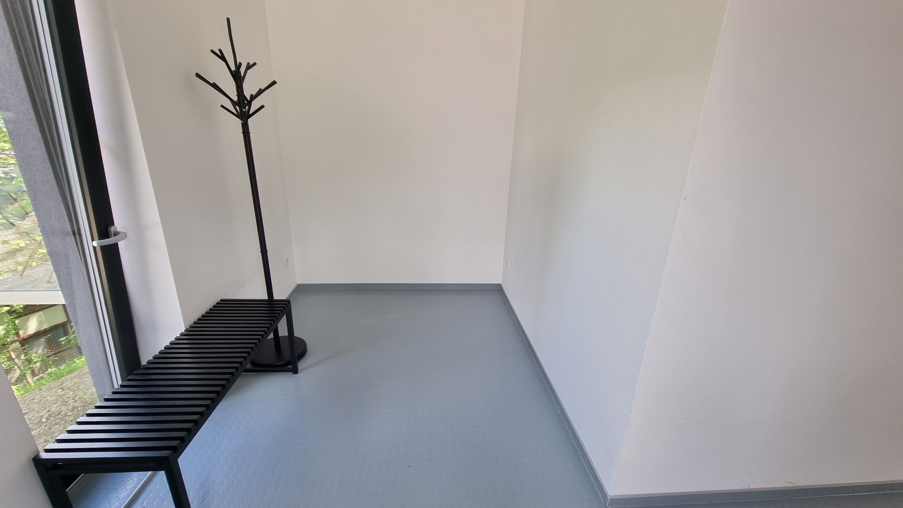 A corner of a room with a bench, a coat rack, and a window.