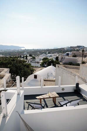 A rooftop terrace with a table and chairs, overlooking a coastal town with white buildings and a clear sky.
