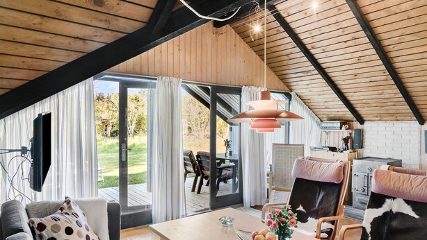 Una sala de estar acogedora con techo de madera, una mesa de comedor con un florero y un ventanal con cortinas.
