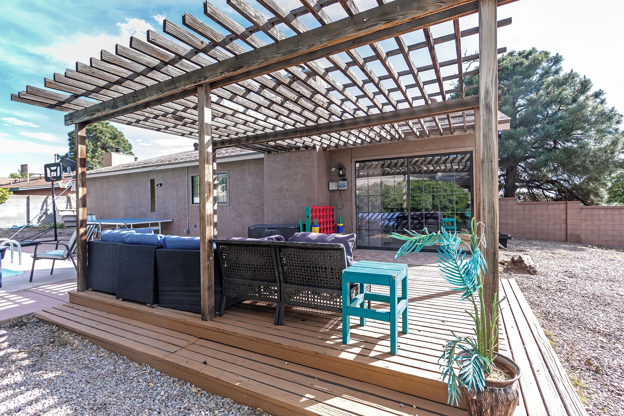 Un patio cubierto con mobiliario exterior, un aro de baloncesto y vistas de la casa a través de una puerta de vidrio.