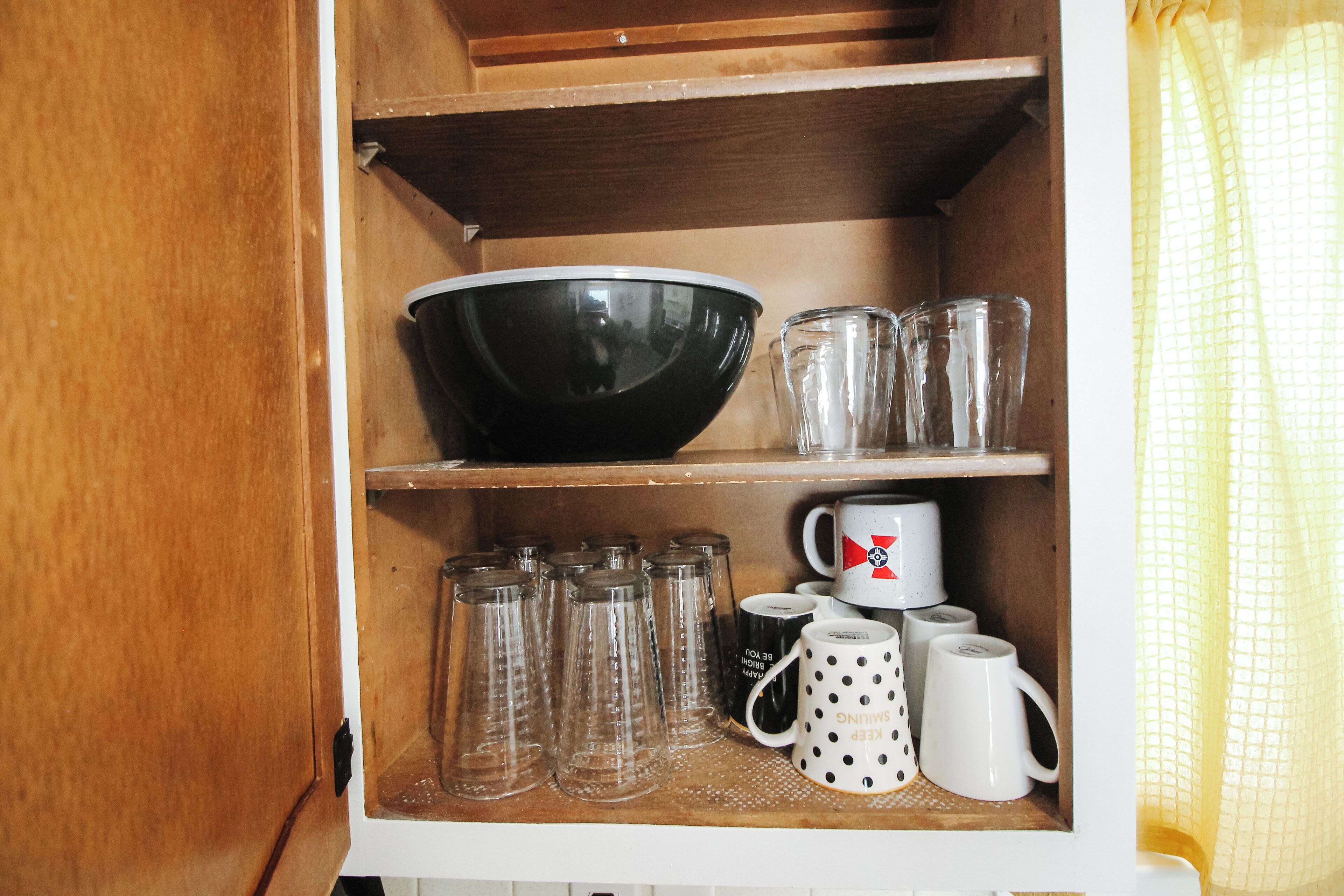 Un meuble de cuisine contenant un saladier noir, des verres à eau transparents et des tasses blanches à pois noirs.