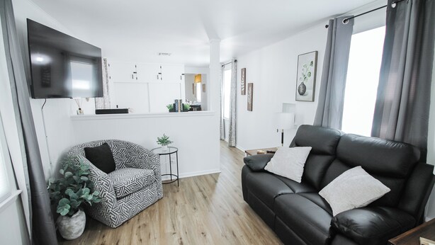Una sala de estar moderna con un sofá de cuero negro, un sillón estampado y un televisor de pantalla plana montado en la pared.