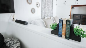 Rincón de lectura ordenado con un sofá blanco, un otoman negro y una estantería llena de libros.