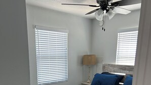 A bedroom with a bed, a ceiling fan, and two windows with blinds. - Sargent Barefoot Bungalow (Bay City)