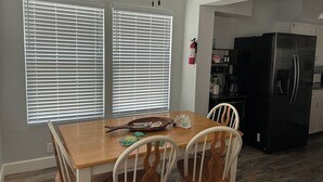 A dining area with a wooden table and white chairs, a black refrigerator, and a ceiling fan. - Sargent Barefoot Bungalow (Bay City)