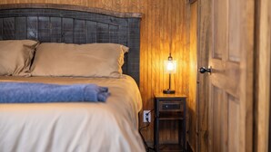 Une pièce aux murs lambrés, comprenant un lit, une table de chevet et une lampe fixée au mur.