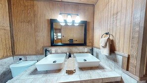 Une salle de bain avec des lambris en bois, deux lavabos, un grand miroir avec éclairage intégré et un porte-serviettes.