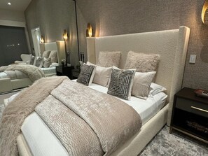 A modern bedroom with a large bed, a nightstand, a mirror, and wall sconces.