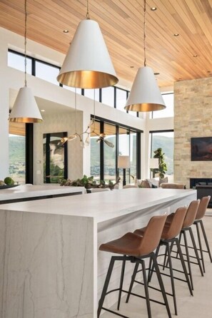 A modern kitchen with a large island, bar stools, pendant lighting, and a view of the outdoors.