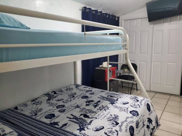A bunk bed room with a patterned bedspread, a desk with a chair, and a wardrobe in the background. - A small, private bedroom & bathroom Little Havana in Miami A1 (Miami)