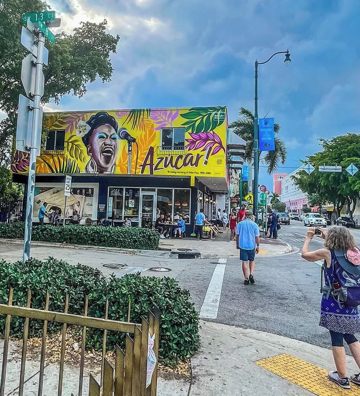 A street corner with a colorful mural on a building, a crosswalk, and a few pedestrians.