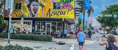 A street corner with a colorful mural on a building, a crosswalk, and a few pedestrians.