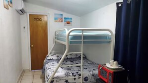 Un llit amb literes amb un estovat estampat, un microones sobre una taula petita, una porta i una cortina.