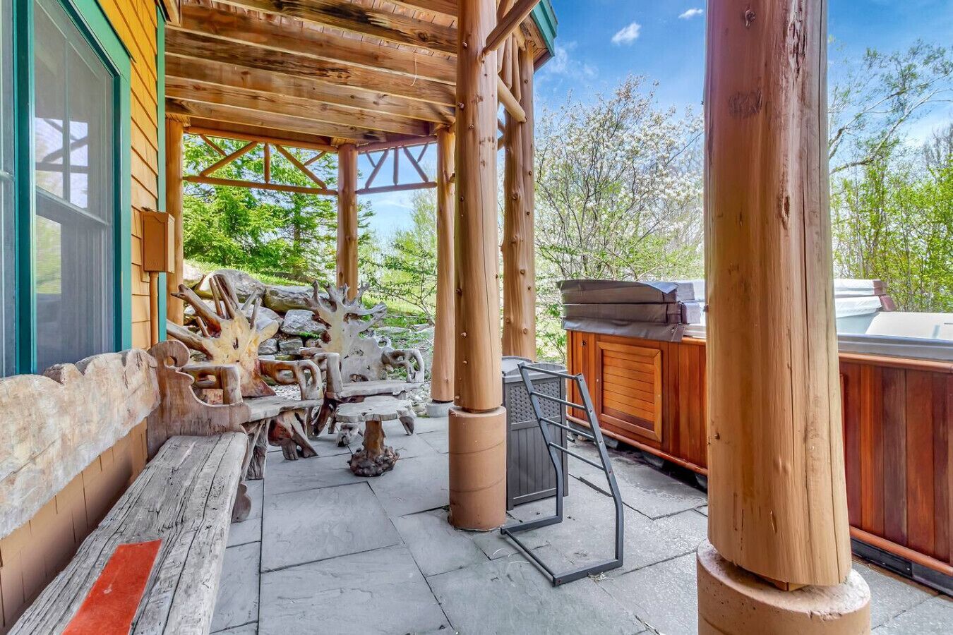 A wooden deck with a covered seating area, a hot tub, and a stone fireplace.