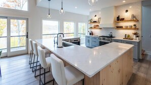 A modern kitchen with a large island, pendant lighting, and a view of autumn trees. - TreeTops, modern luxury overlooking Keuka Lake - Luxury Treehouse included (Penn Yan)