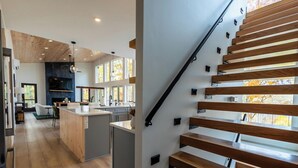 A modern kitchen with a central island, wooden staircase, and large windows. - TreeTops, modern luxury overlooking Keuka Lake - Luxury Treehouse included (Penn Yan)