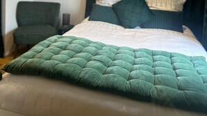 Ein Bett mit dunklem Kopfteil, einer grünen Steude und zwei Kissen.