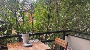 Ein Holztisch mit Kissen und einer Topfpflanze auf einem Balkon mit Geländer.