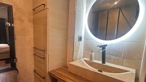 Ein Badezimmer mit einem Holzkosmetikschrank, einem runden Spiegel mit Beleuchtung und einem Waschbecken.