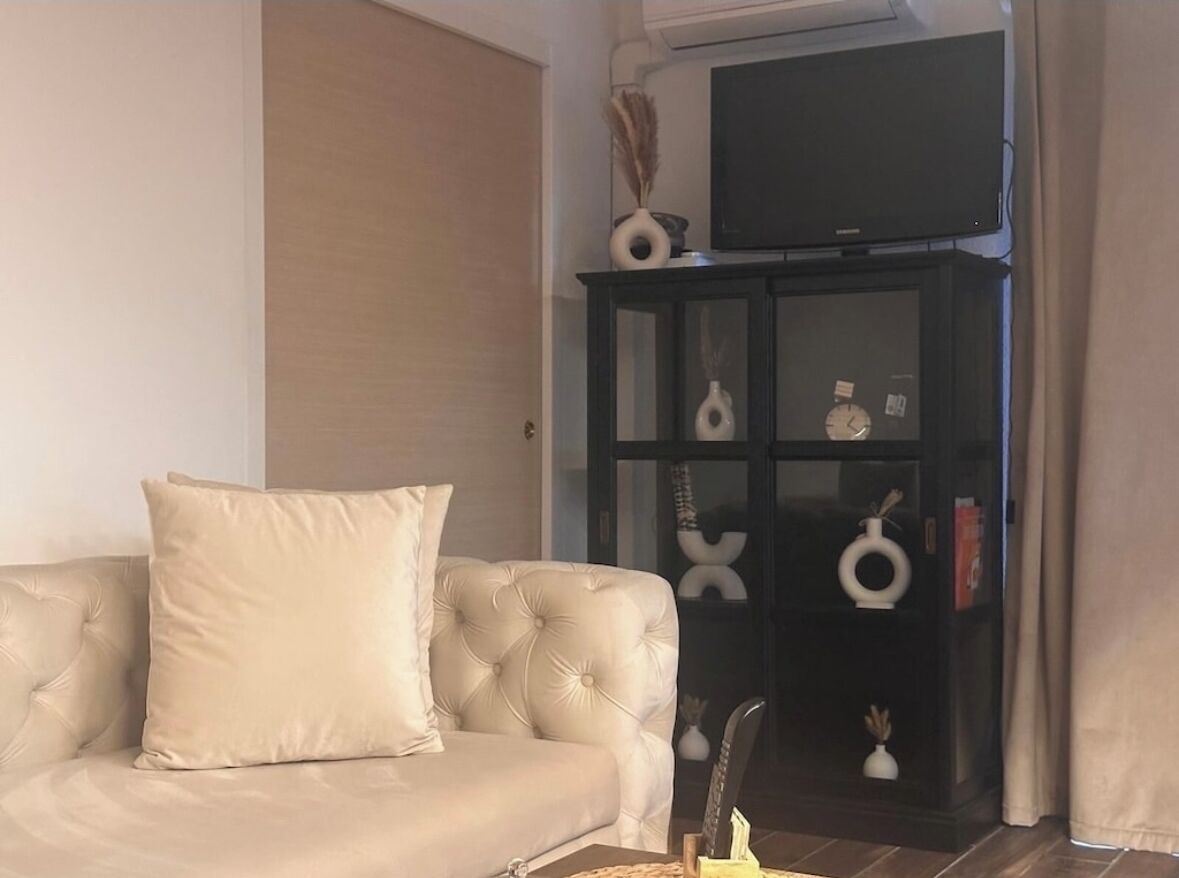 Un salon avec un canapé beige, un meuble sombre agrémenté d’objets décoratifs et un téléviseur posé sur le dessus.