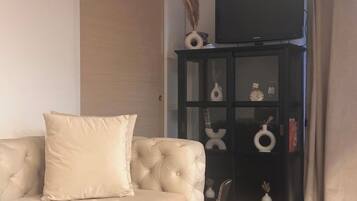 Un salon avec un canapé beige, un meuble sombre agrémenté d’objets décoratifs et un téléviseur posé sur le dessus.